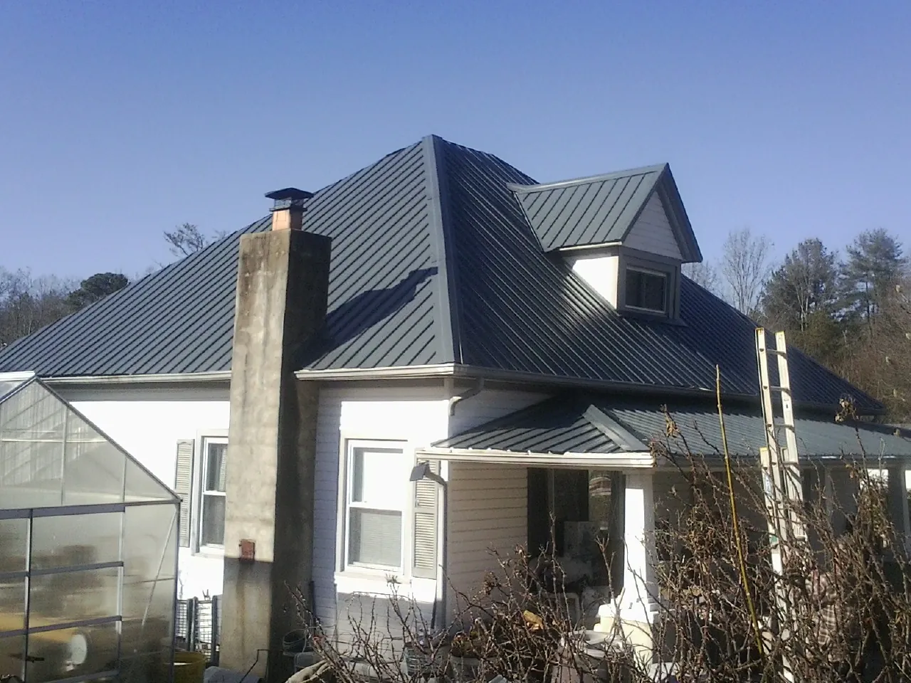 Dark blue standing seam metal roof on a white farmhouse with dormer — Slate & Tile Roof Repair by Roofing Brothers in Bridgeview