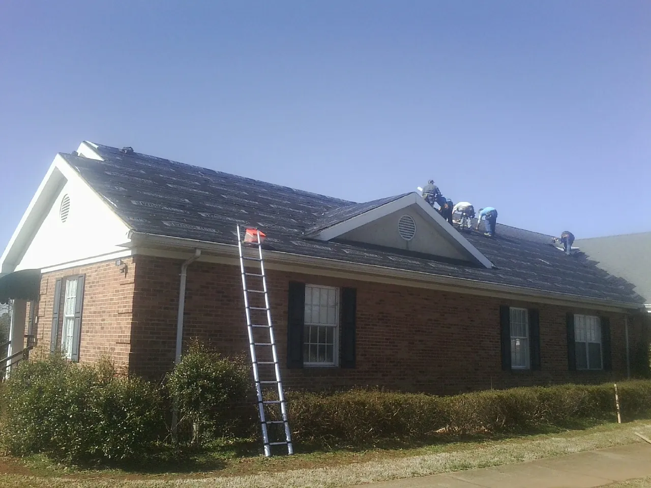 Crew tearing shingles off a brick ranch roof with a ladder set — Metal Roof Repair work by our crew in Bridgeview