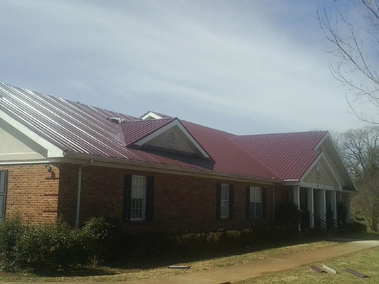 Red metal roof with gabled entries on a long brick building, from a Hail Damage Roof Repair job in Bridgeview