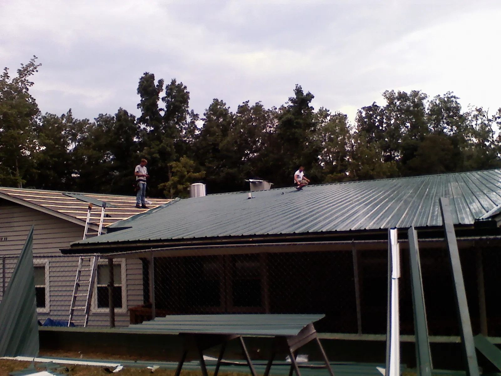Two roofers installing green metal panels above a covered porch in Bridgeview