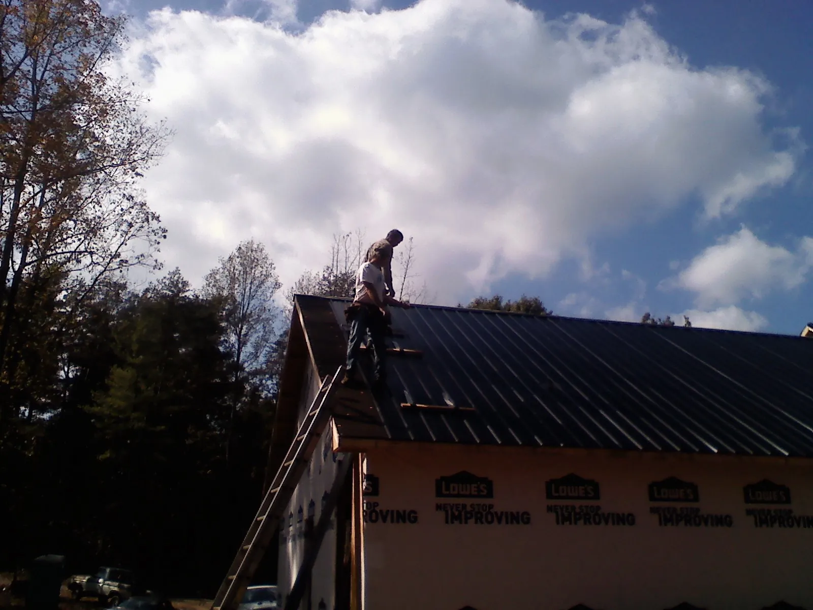 Roofer fastening dark metal panels high against a cloudy sky, from a Roof Inspection job in Bridgeview